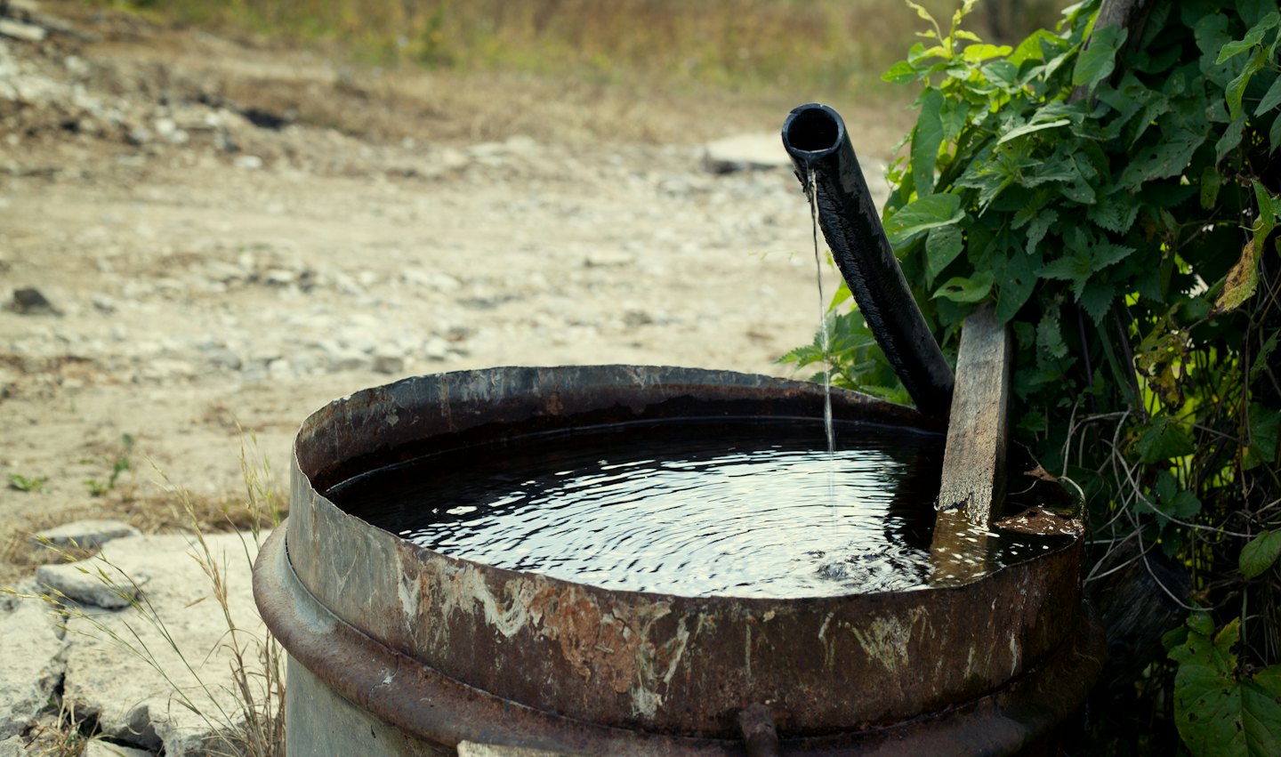 Water pours from a pipe into a rustic metal trough.