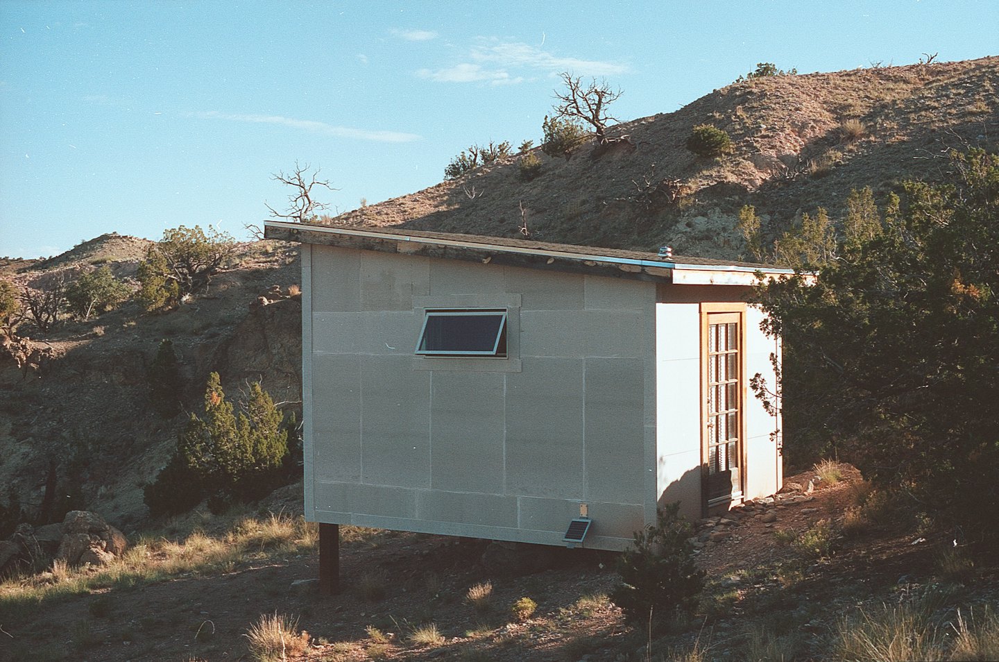 Small off-grid cabin with a solar panel on a rocky hillside.
