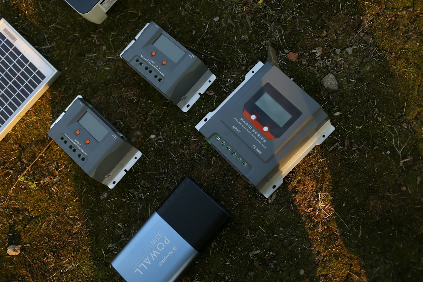 Solar charge controllers, panel, and power bank on grass.