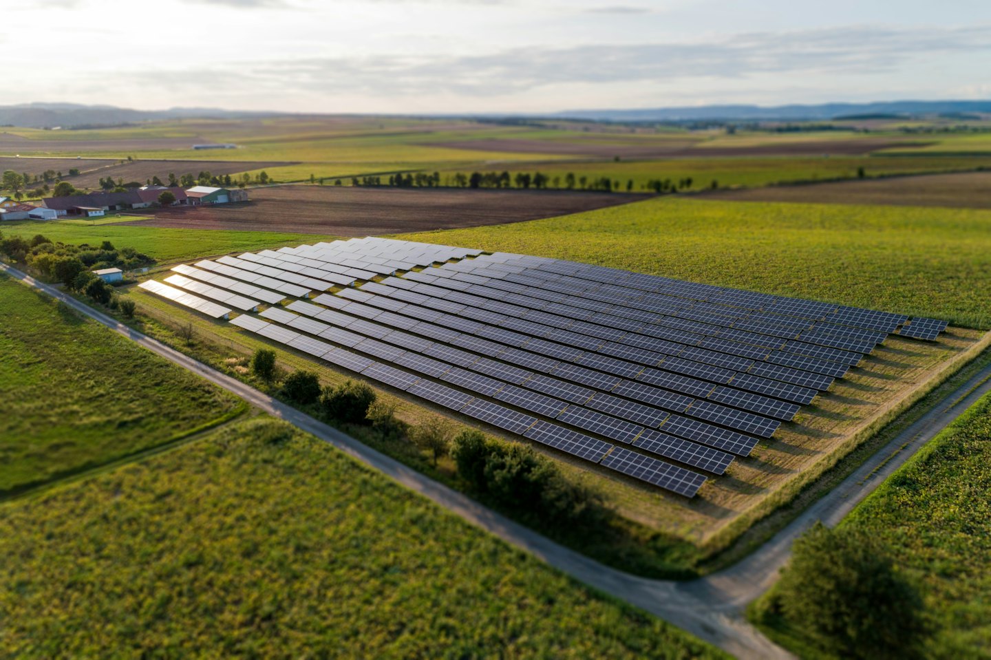 Solar panels cover a field near farm buildings.